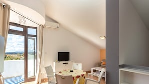 A dining area with a table and chairs, a television, and a view through a glass door. - Apartments Ilija Njavro (Crikvenica)