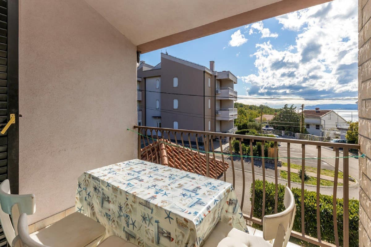 Un balcón con mesa y sillas, vista a un edificio y cielo despejado.