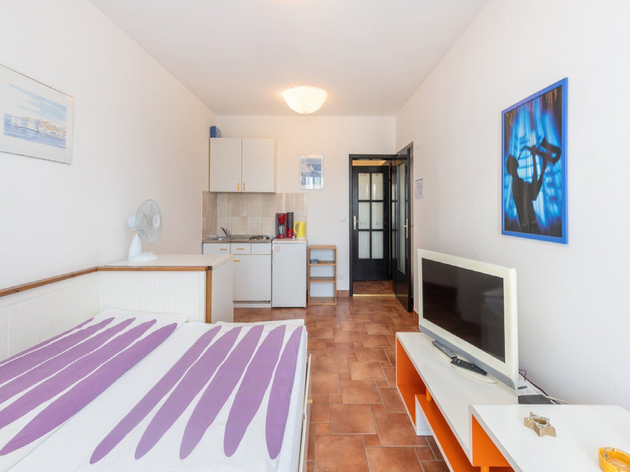 A compact hotel room with a bed, a TV, a kitchenette, and a bathroom visible through an open door.
