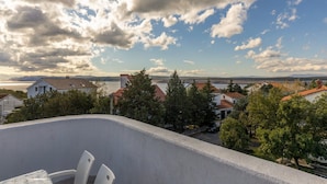 A balcony with a view of a lake, houses, and trees. - Apartments Ilija Njavro (Crikvenica)