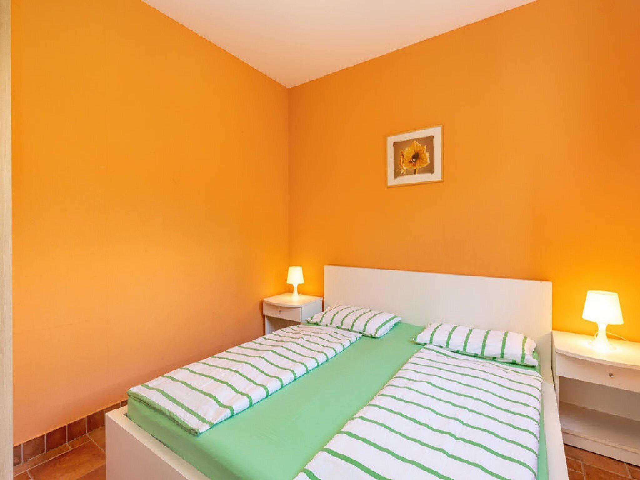 A single bed with a green and white striped bedspread, two bedside tables with lamps, and a small framed picture on the wall.