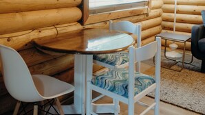 A cozy log cabin interior with a dining table, two chairs, a window with blinds, and a lamp. - Tranquil cabin with WiFi in charming Wasilla (Wasilla)