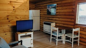 A cozy cabin interior with a wooden interior, a television on a small table, a refrigerator, and a window with blinds. - Tranquil cabin with WiFi in charming Wasilla (Wasilla)