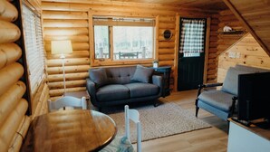 A cozy log cabin interior with a sofa, a small table, and a chair. - Tranquil cabin with WiFi in charming Wasilla (Wasilla)