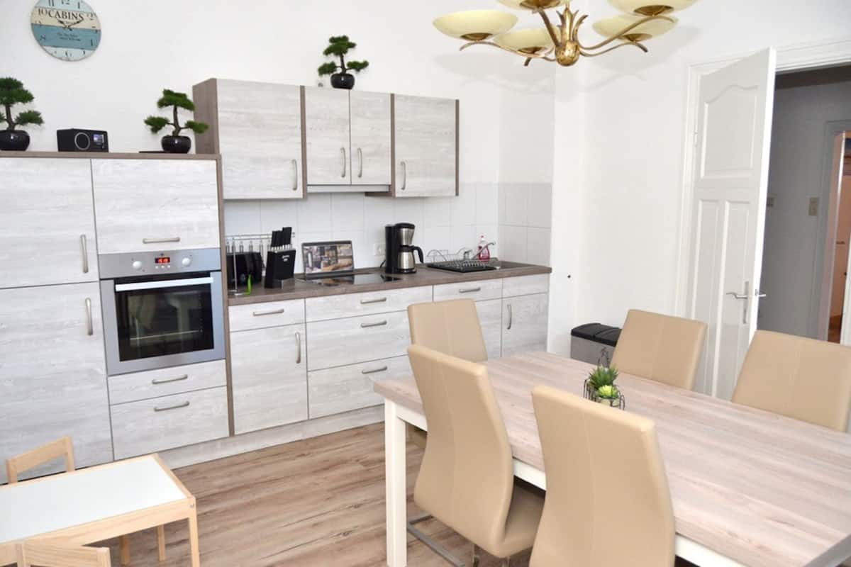 A modern kitchen with a built-in oven, a coffee maker, and a dining area with a wooden table and chairs.