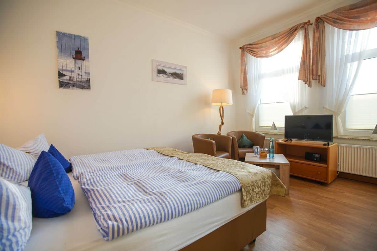 A hotel room with a bed, a desk with a lamp, a TV, and a chair.
