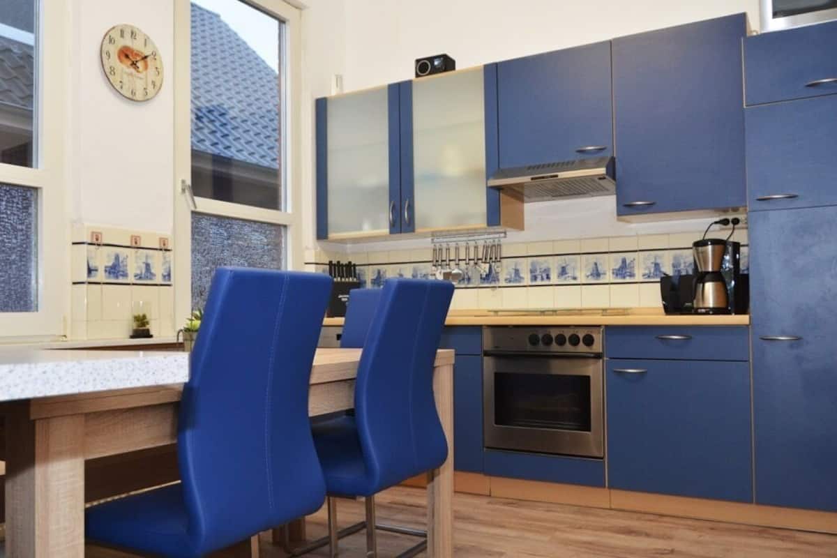 A kitchen with blue cabinets, a stove, and a clock on the wall.