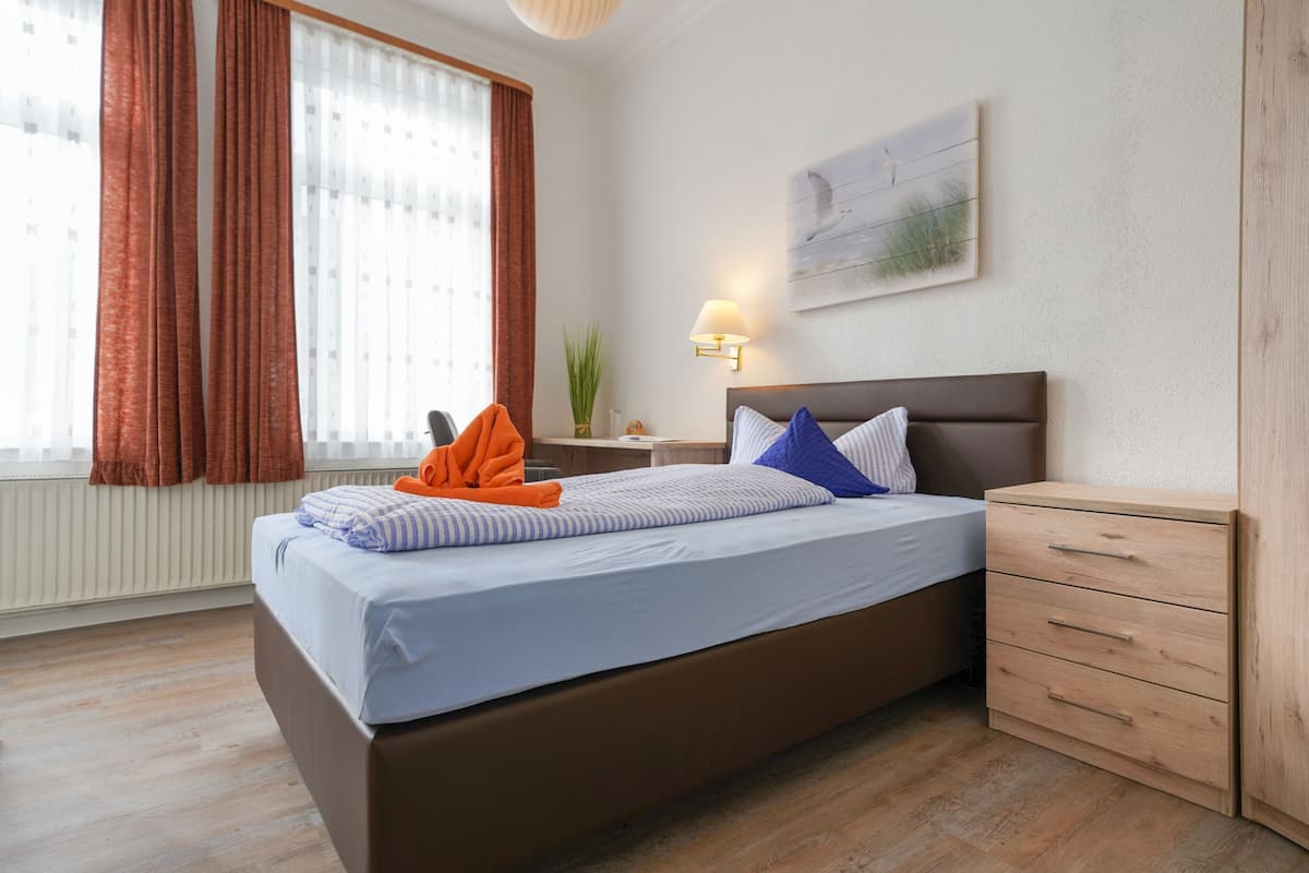 A bedroom with a bed, a nightstand, a lamp, a painting, and a wooden cabinet.