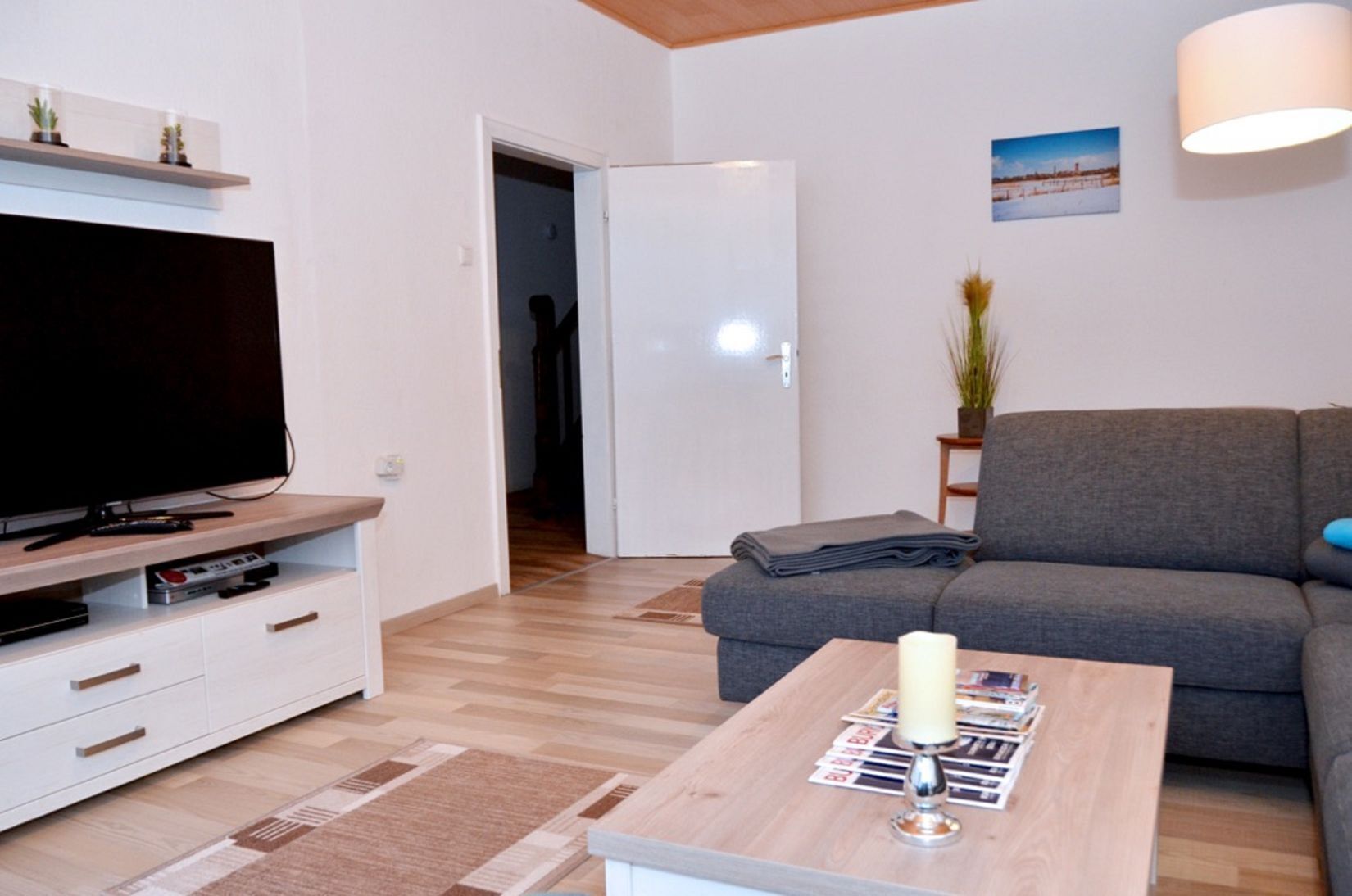 Un salon moderne avec un téléviseur à écran plat, un canapé gris, une table basse en bois et une petite table d’appoint avec une lampe.