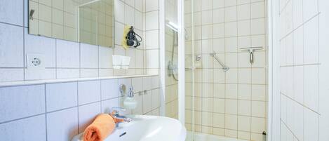 A bathroom with a sink, mirror, and shower.