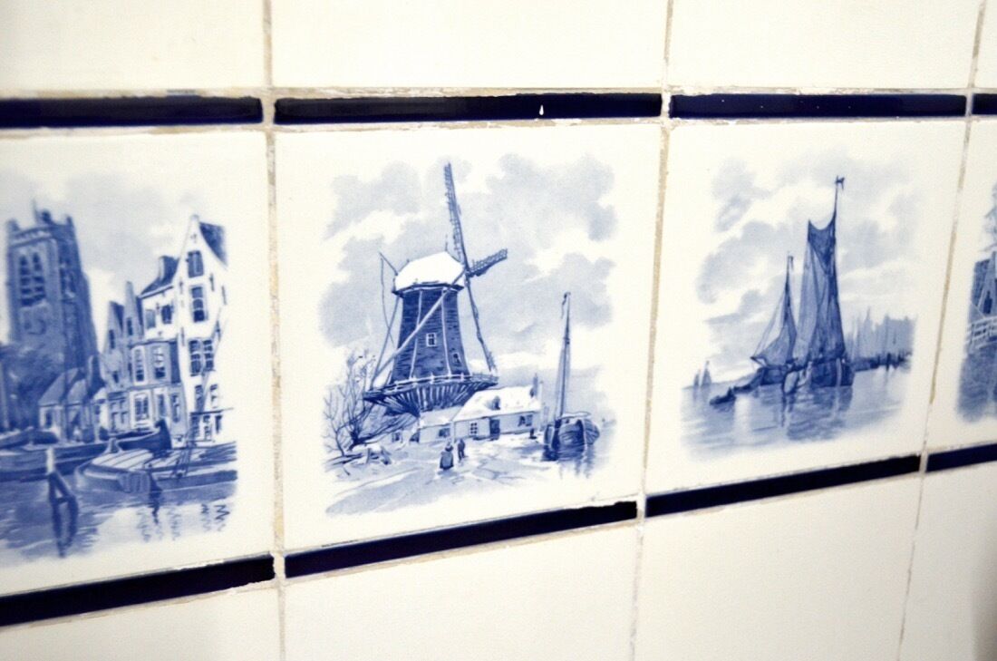 A tiled wall with blue and white illustrations of a windmill, a sailboat, and buildings.
