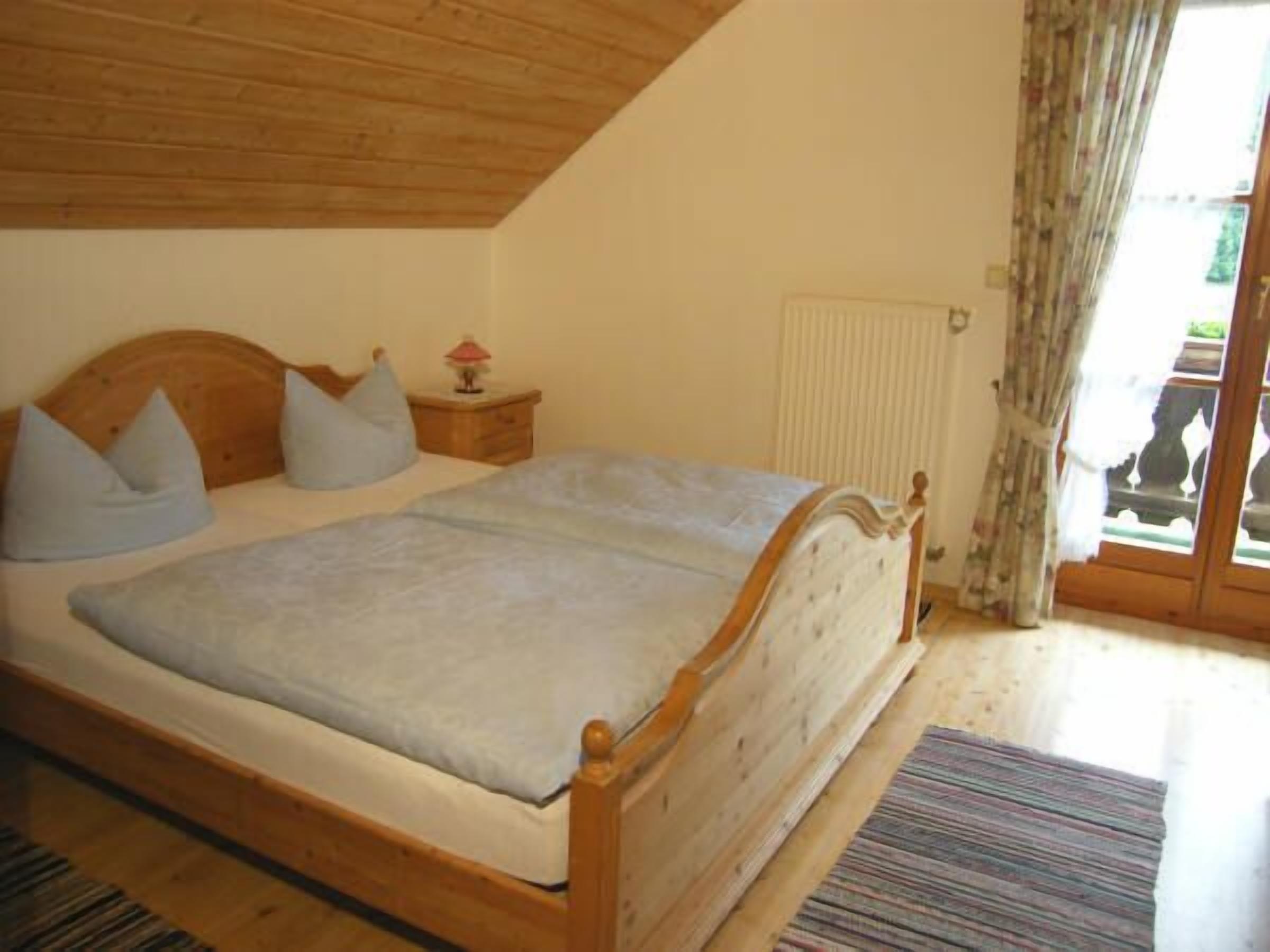 A bedroom with a wooden bed, a nightstand, a lamp, and a window with curtains.