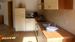 A compact kitchen with a microwave, sink, and wooden cabinets. - Bergblick94m², EG, 2 Schlafzimmer, Sat-tv, Terrasse, Max. 4 Personen (Anger)