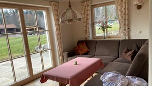 A living room with a sofa, a table with a pink tablecloth, a hanging light fixture, and a window with curtains. - Bergblick94m², EG, 2 Schlafzimmer, Sat-tv, Terrasse, Max. 4 Personen (Anger)