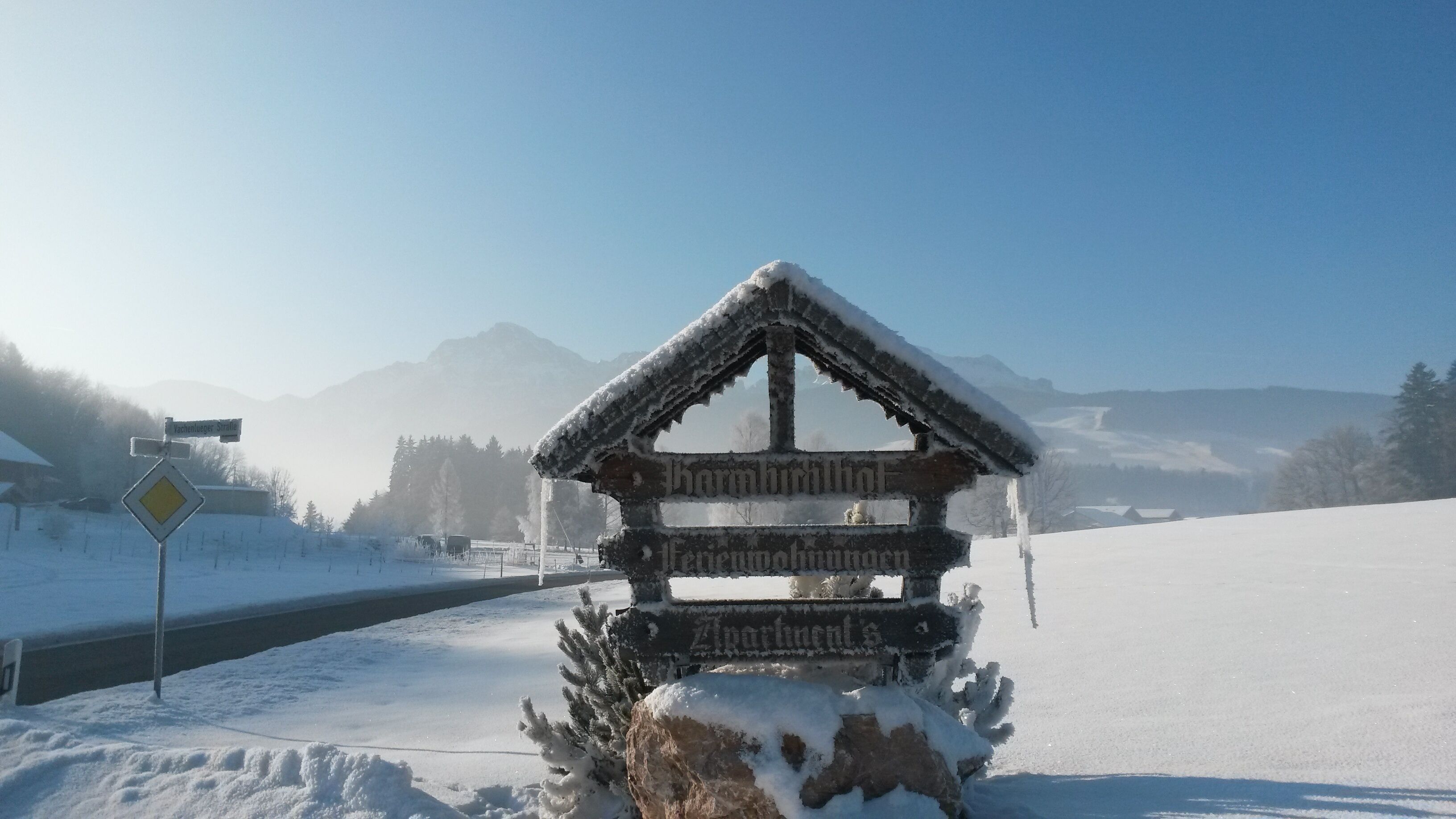 Un letrero de madera cubierto de nieve con la palabra 'Zahnwirt' y 'Fennwiesenhof' escrito, que señala una posada o casa de huéspedes local.