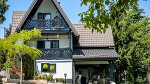 Una casa de dues plantes amb teulada fosca i parets blanques, amb un balcó a la planta superior.
