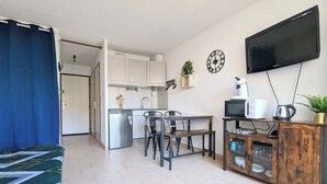 A compact living space with a kitchenette, a dining area, a TV mounted on the wall, and a small cabinet with kitchen appliances. - Apartment in Agde (Agde)