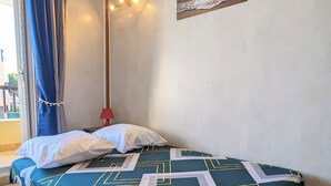 A neatly made bed with a geometric patterned bedspread, a single red bedside lamp, and a wall-mounted painting of a sunset over the ocean. - Apartment in Agde (Agde)