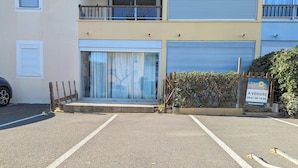 A parking lot with a building entrance, a signboard, and a wooden fence. - Apartment in Agde (Agde)