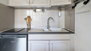 A compact kitchen with white cabinets, a stainless steel dishwasher, and a sink with a faucet. - Apartment in Agde (Agde)