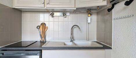 A compact kitchen with white cabinets, a stainless steel dishwasher, and a sink with a faucet.