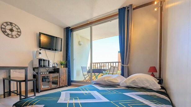 A bedroom with a bed, a desk with a computer, a TV, and a balcony with a chair. - Apartment in Agde (Agde)
