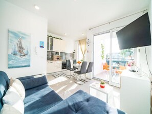 Uma sala de estar moderna com um sofá, uma TV de tela plana e um espaço de refeições com cadeiras e uma mesa.