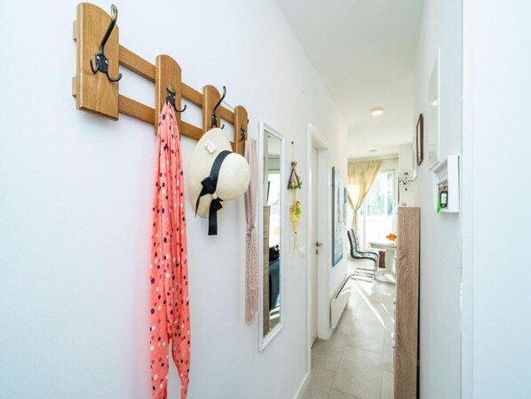 A hallway with a coat rack holding a hat and a polka-dotted garment. A chair is visible in the background, and a door leads to another room. - Apartment Anka (Dubrovnik)