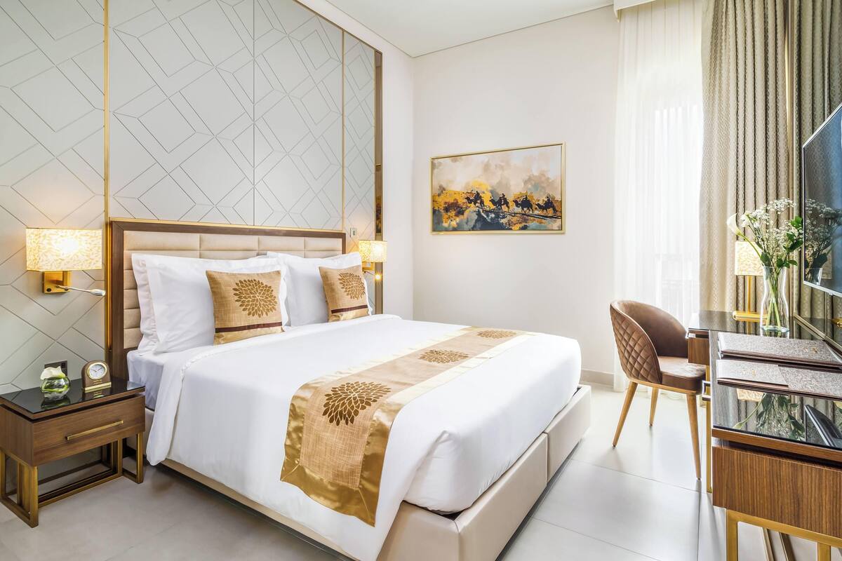A hotel room with a large bed, a desk with a chair, a nightstand, and a wall-mounted TV.