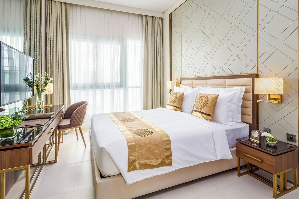A hotel room with a large bed, a desk with a chair, a TV, and a lamp.