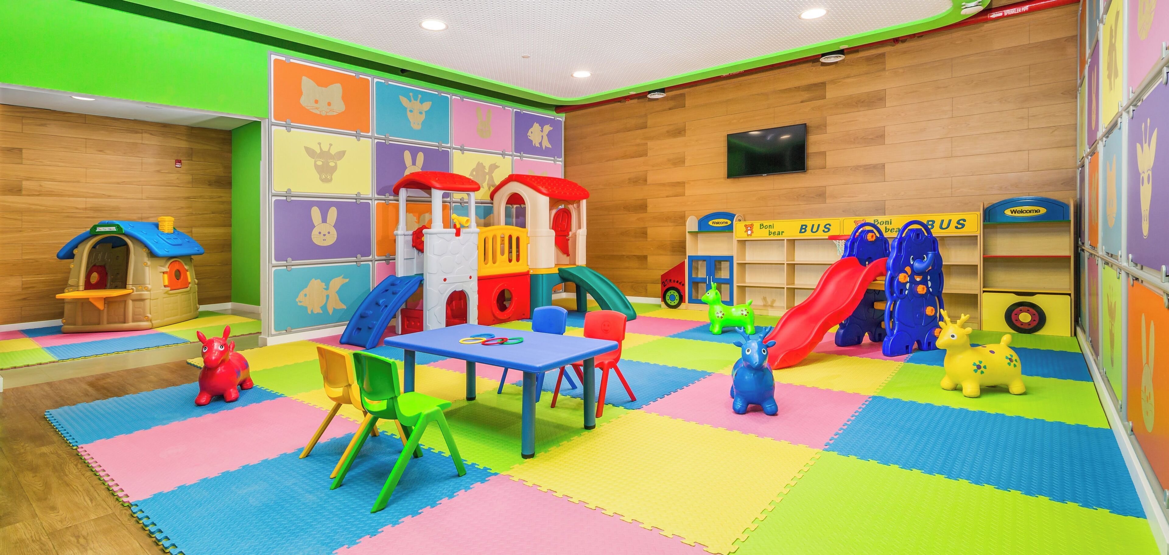 Zona de juegos infantiles con una casita, toboganes y colchonetas de colores.