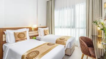 A hotel room with two beds, a nightstand, a chair, and a large window with curtains.