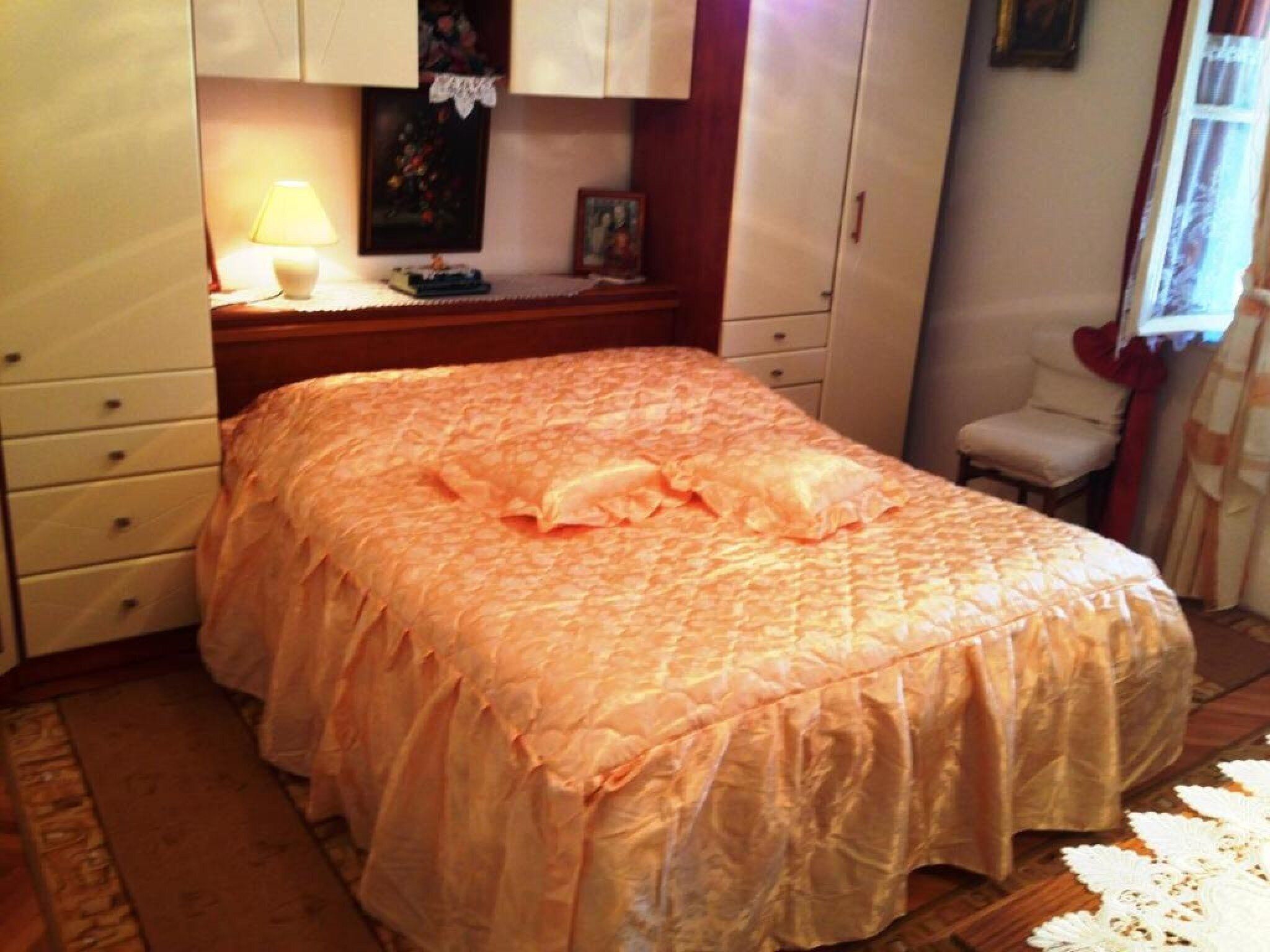 Een slaapkamer met een bed, nachtkastje, lamp en stoel.