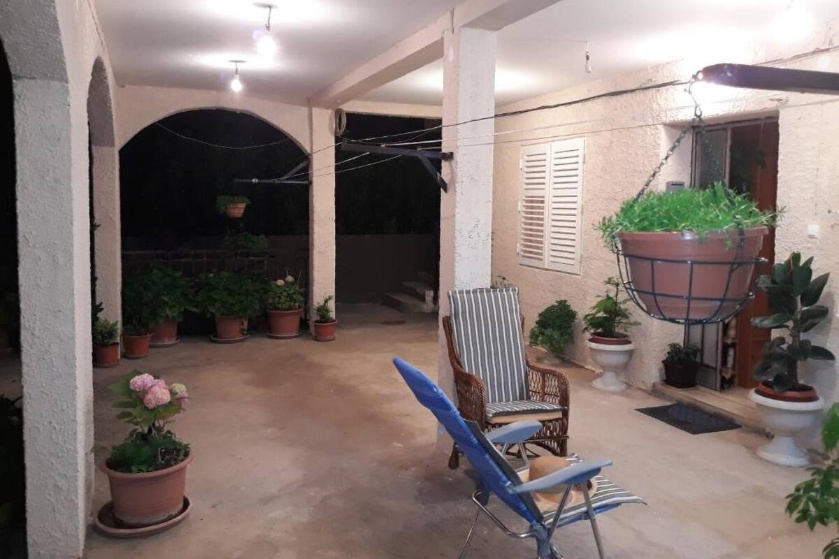 A covered patio area with potted plants, a blue chair, and hanging planters.