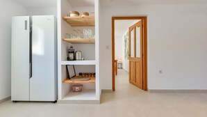 Een moderne keuken met een geïntegreerde koelkast, houten planken en een zichtbare eethoek door een open deur.