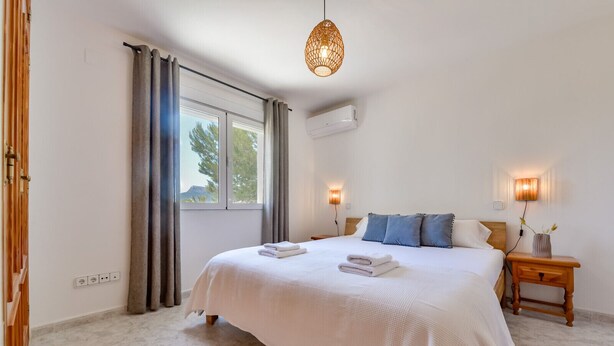 Een slaapkamer met een groot bed, twee bedlampen, een nachtkastje en een raam met gordijnen.