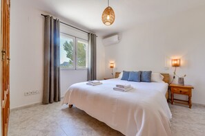 Een slaapkamer met een groot bed, twee bedlampen, een nachtkastje en een raam met gordijnen.