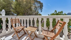 Een balkon met twee houten stoelen en een tafel, omringd door een witte balustrade, met uitzicht op een bergachtig landschap.