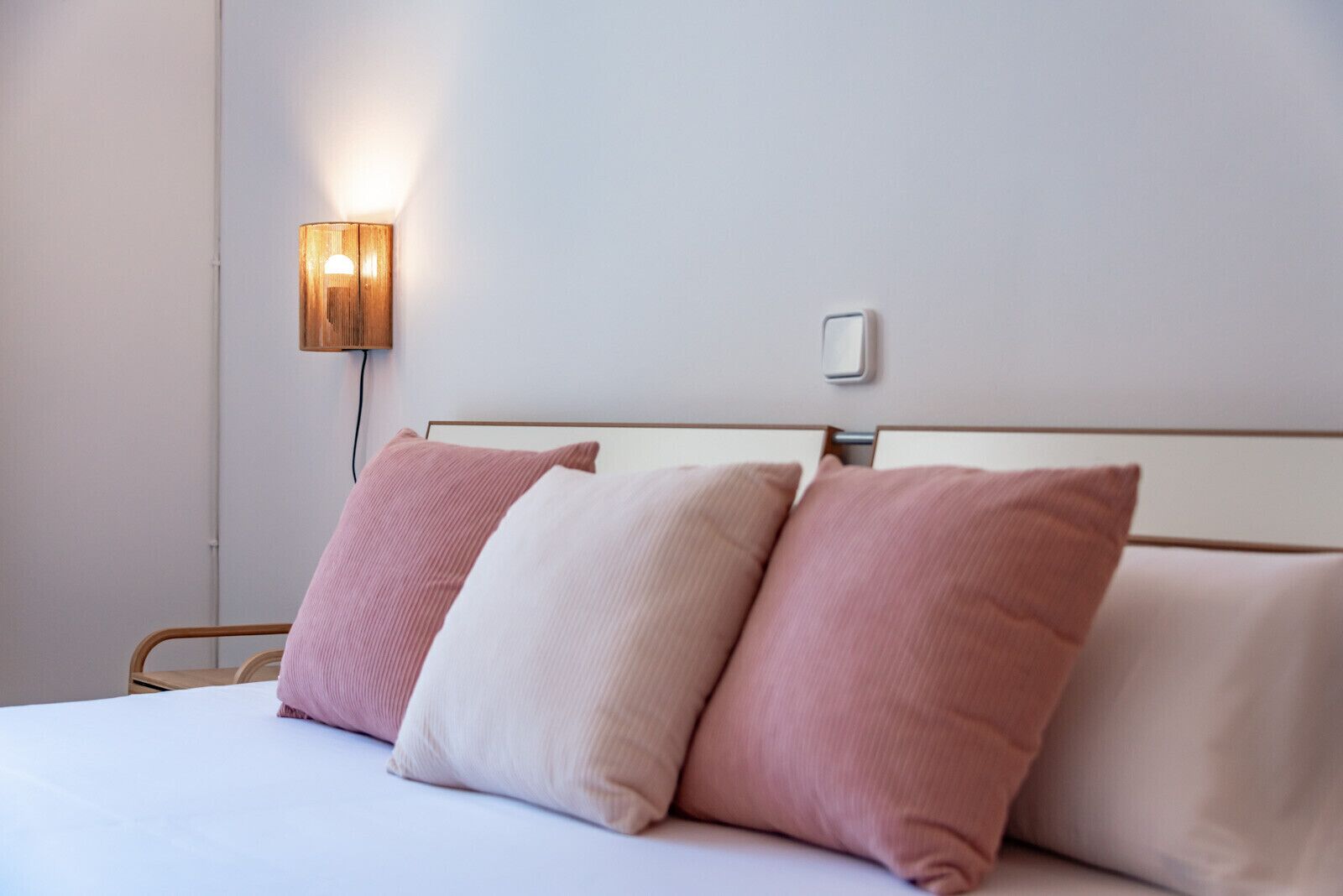 Een net opgemaakt bed met drie kussens, een wandlamp en een stopcontact.