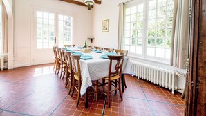 A dining room with a large table set for six, wooden chairs, a white tablecloth, and a view of the outdoors through large windows. - Keravel, family home with character and direct access to the sea (Tréflez)