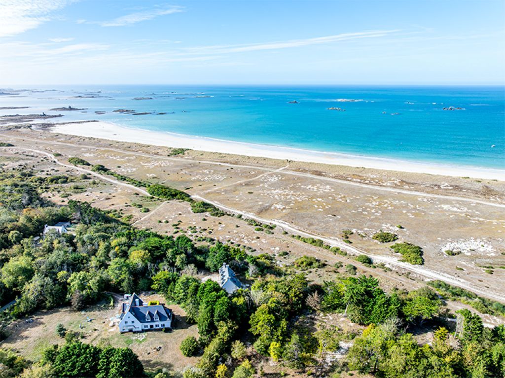 Luftaufnahme eines Anwesens an der Küste, mit Strand, einem großen Haus und umliegender Vegetation.