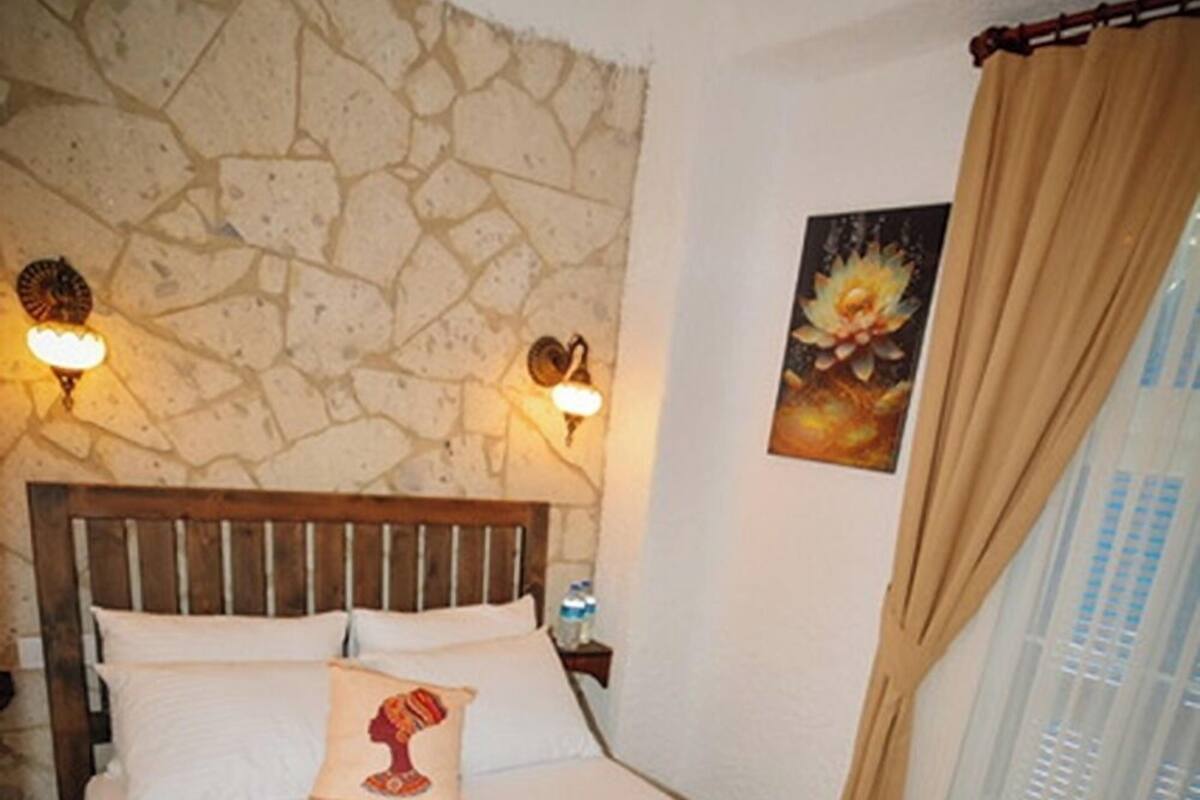 Un lit avec une tête de lit en bois, deux lampes fixées au mur, un seul oreiller et un tableau accroché au mur.