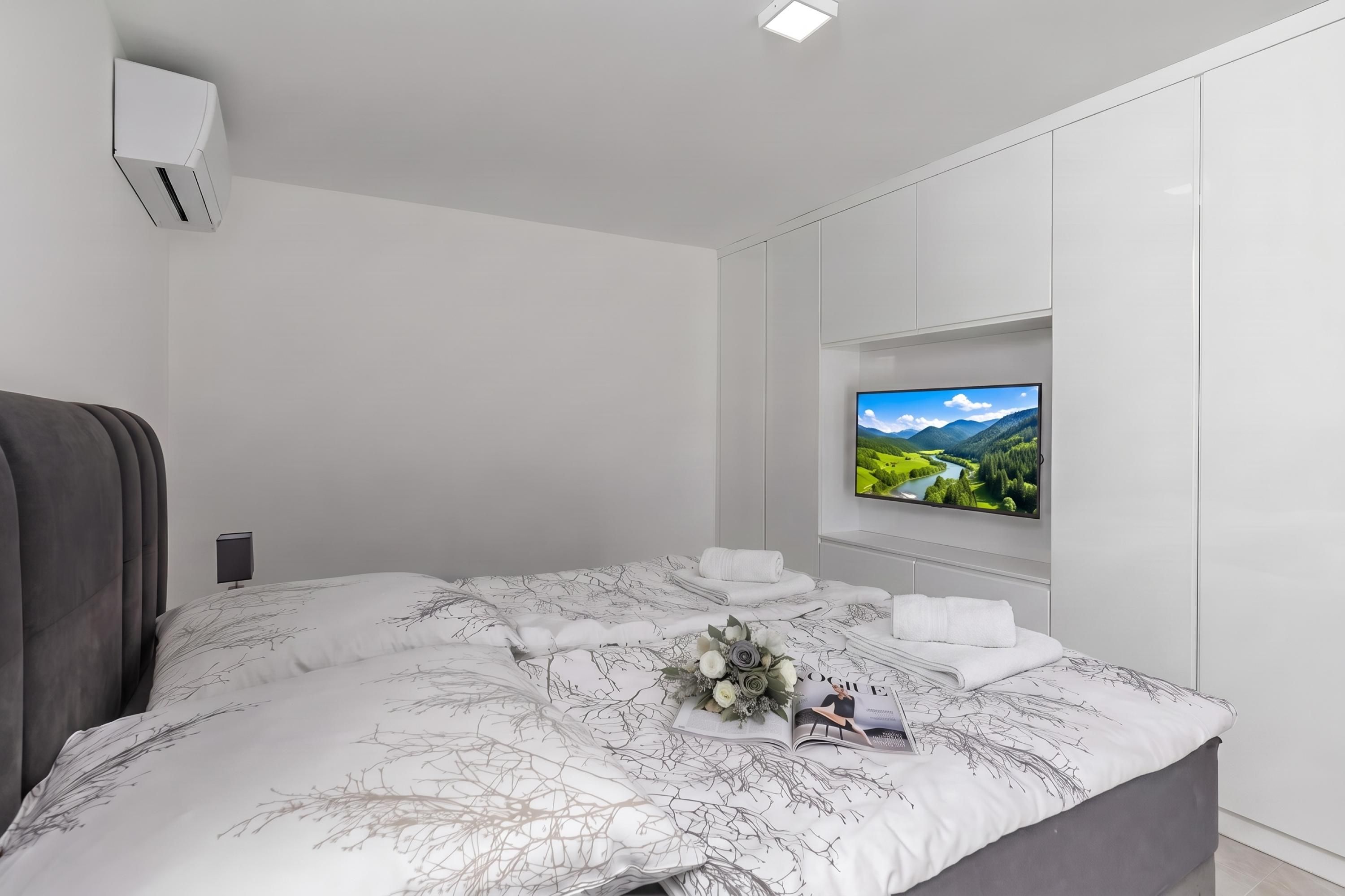 Un dormitorio moderno con una cama grande, un televisor montado y un equipo de aire acondicionado integrado.