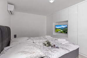 Un dormitorio moderno con una cama grande, un televisor montado y un equipo de aire acondicionado integrado.