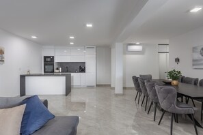 Contemporary kitchen with a central island, appliances, and a dining area with a large table and grey upholstered chairs.