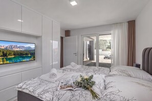 Een moderne slaapkamer met een groot bed, een televisie aan de muur en uitzicht op een bergachtig landschap.