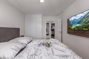 A bedroom with a bed, a wardrobe, a bathroom visible through an open door, and a large landscape painting on the wall. - Spacious Pool Apartment Crikvenica (Crikvenica)