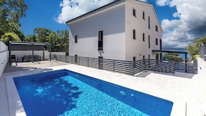 Ein modernes Gebäude mit Schwimmbad, Sitzgelegenheiten im Freien und Meerblick.