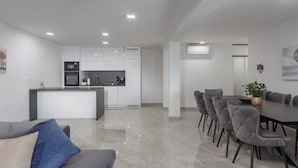 Eine moderne Küche mit weißen Schränken, einer zentralen Kochinsel und einem Essbereich mit grau gepolsterten Stühlen und einem Tisch.