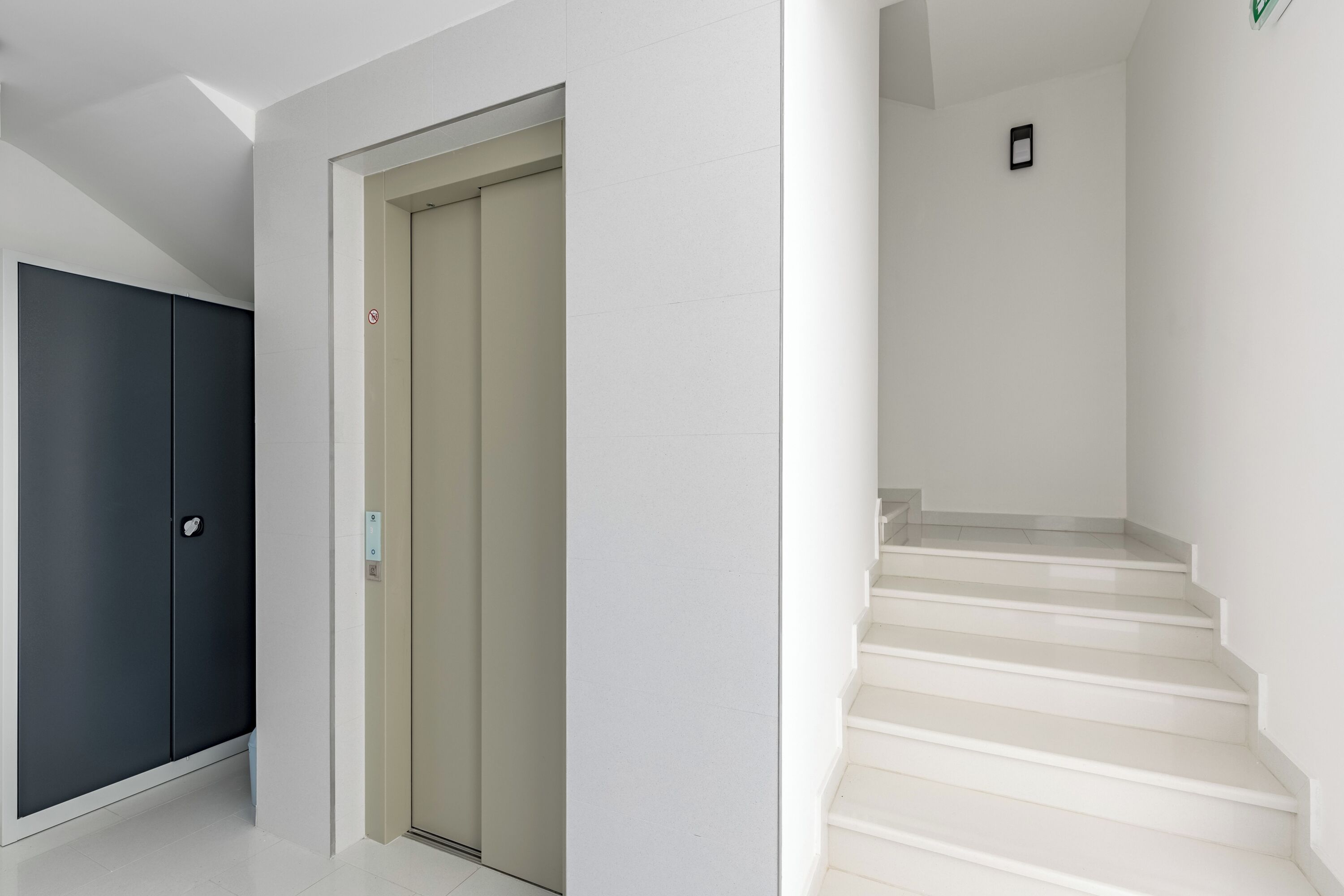 A hallway with a dark-colored wardrobe, a beige door, and a staircase leading to an upper floor.